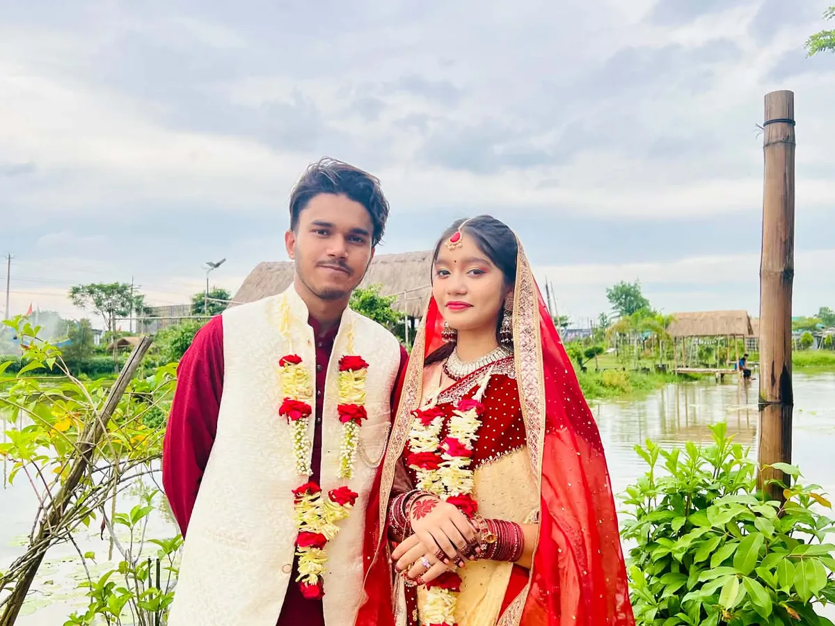 The couple standing side by side with flower garlands by a pond