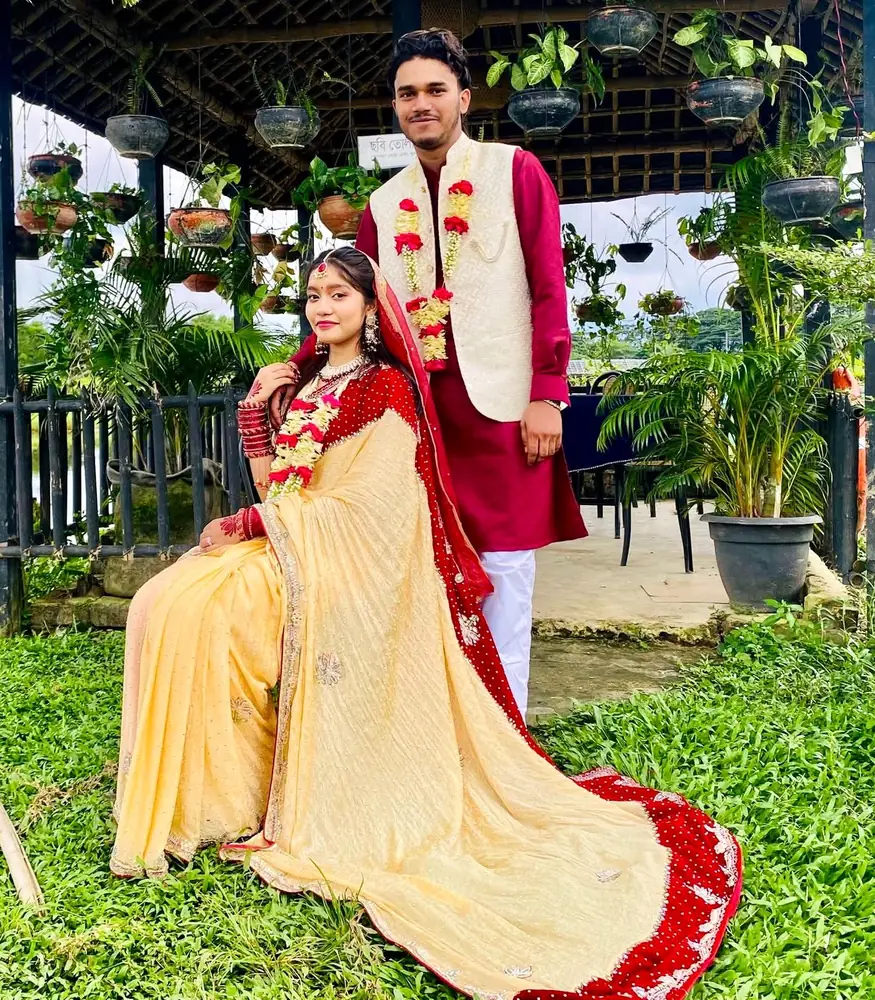 The bride seated in a flowing saree, the groom standing behind her under a garden gazebo
